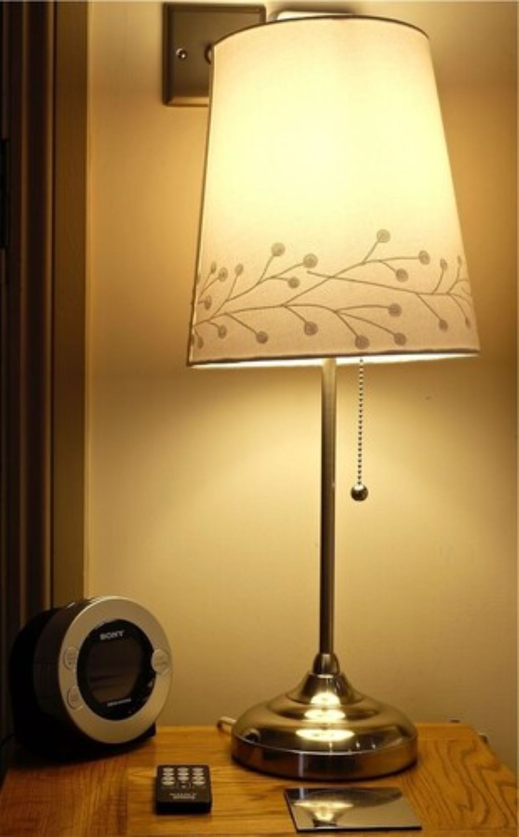 A bedside table with a lamp, a remote control, and a clock.