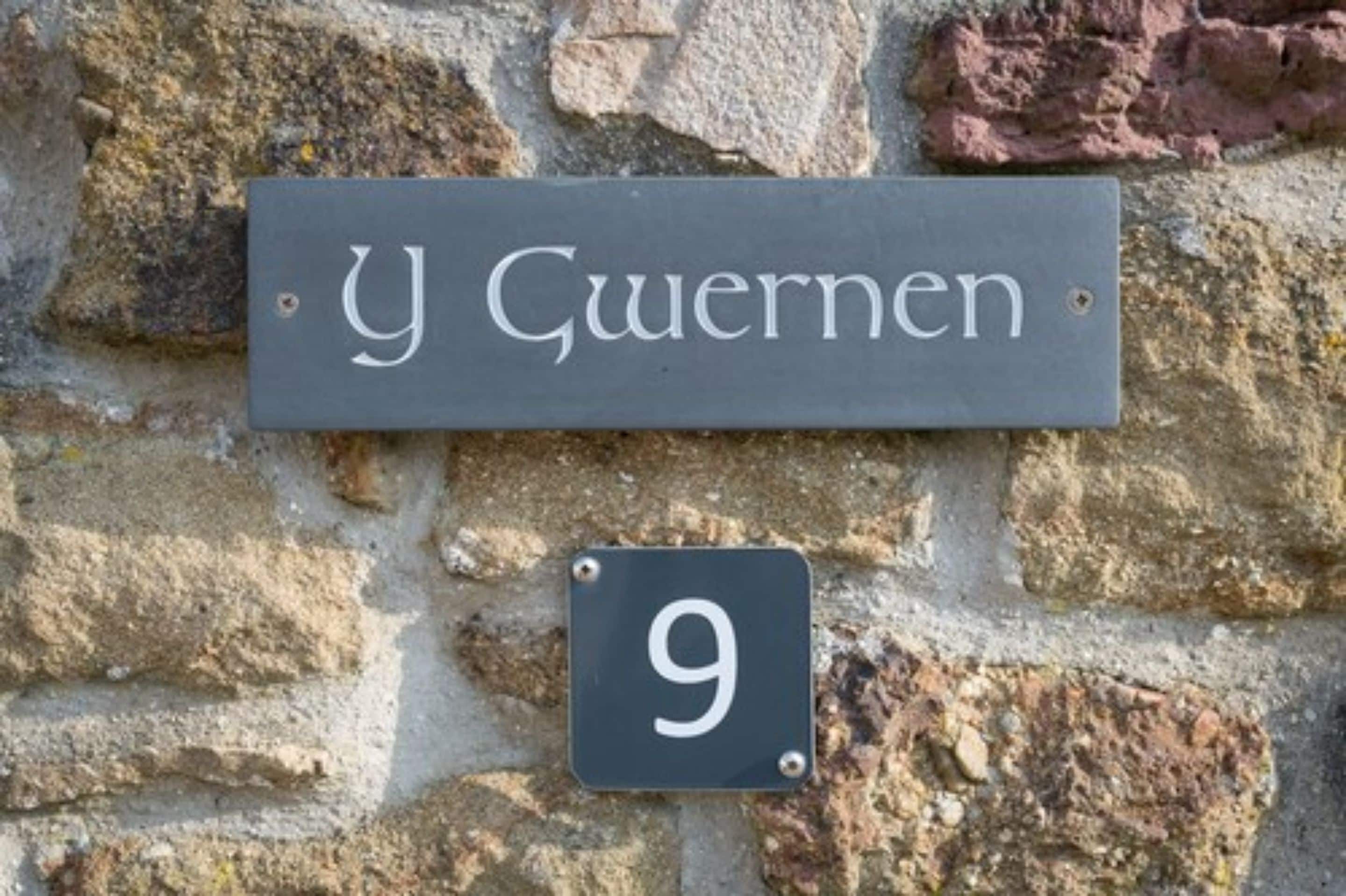 A house number sign with '9' and a street name sign reading 'y Gwernen' mounted on a stone wall.