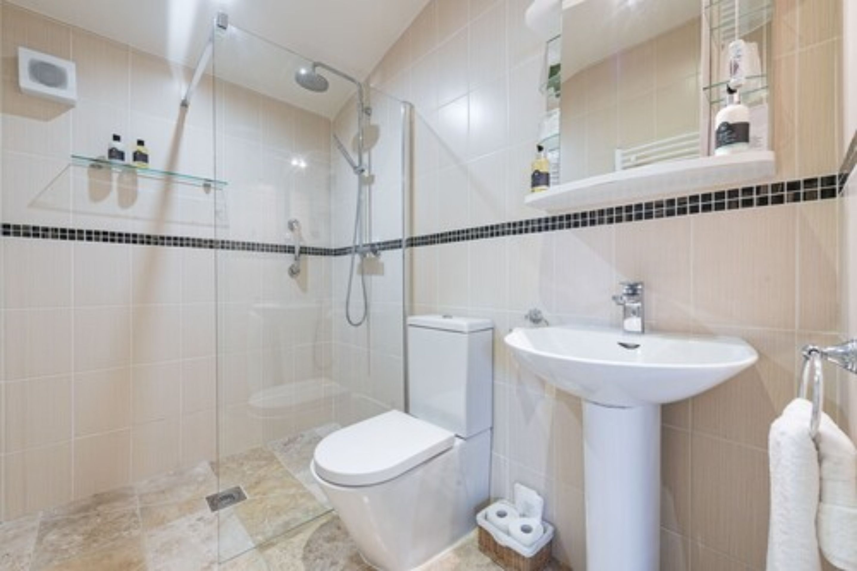 A modern bathroom with a glass shower enclosure, a white toilet, and a pedestal sink.