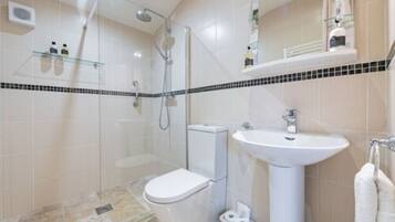 A modern bathroom with a glass shower enclosure, a white toilet, and a pedestal sink.