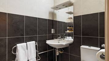 Un baño moderno con baldosas oscuras, un lavamanos blanco, un inodoro y un perchero con dos toallas.