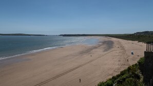A wide sandy beach with a clear blue sky, a few people walking, and a distant view of hills. - Canaston Oaks (Narberth)