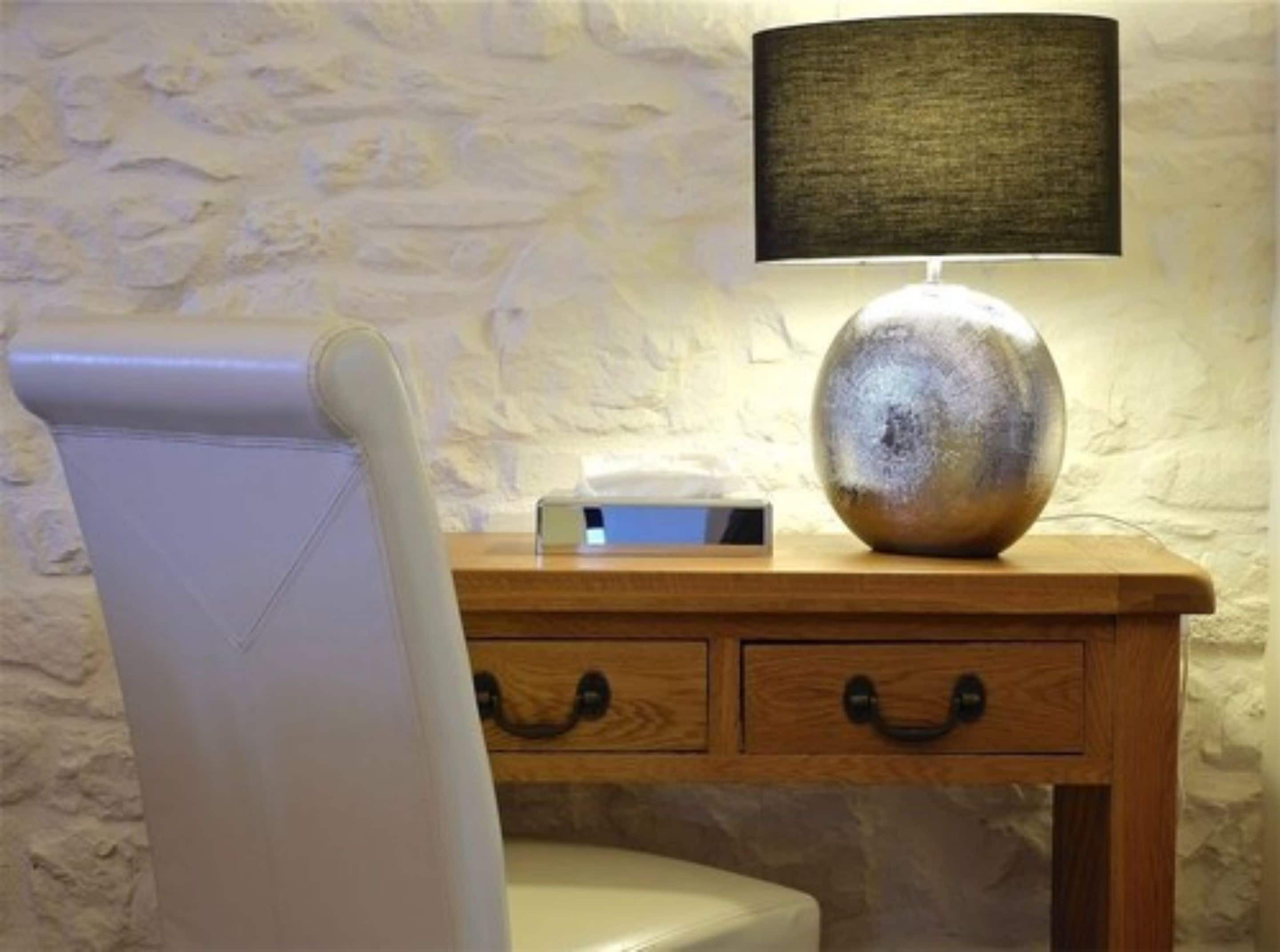 Une chaise blanche avec un dossier incurvé, une table de chevet en bois avec une lampe, et un mur orné d’un motif texturé.