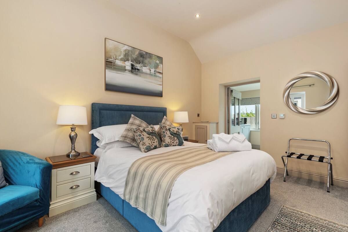 A bedroom with a bed, nightstands, a blue chair, a mirror, and a painting on the wall.