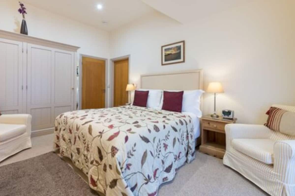 A bedroom with a large bed, two bedside tables, a wardrobe, and two armchairs.