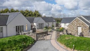 A row of white buildings with grey roofs, a gravel path, and green landscaping. - Canaston Oaks (Narberth)