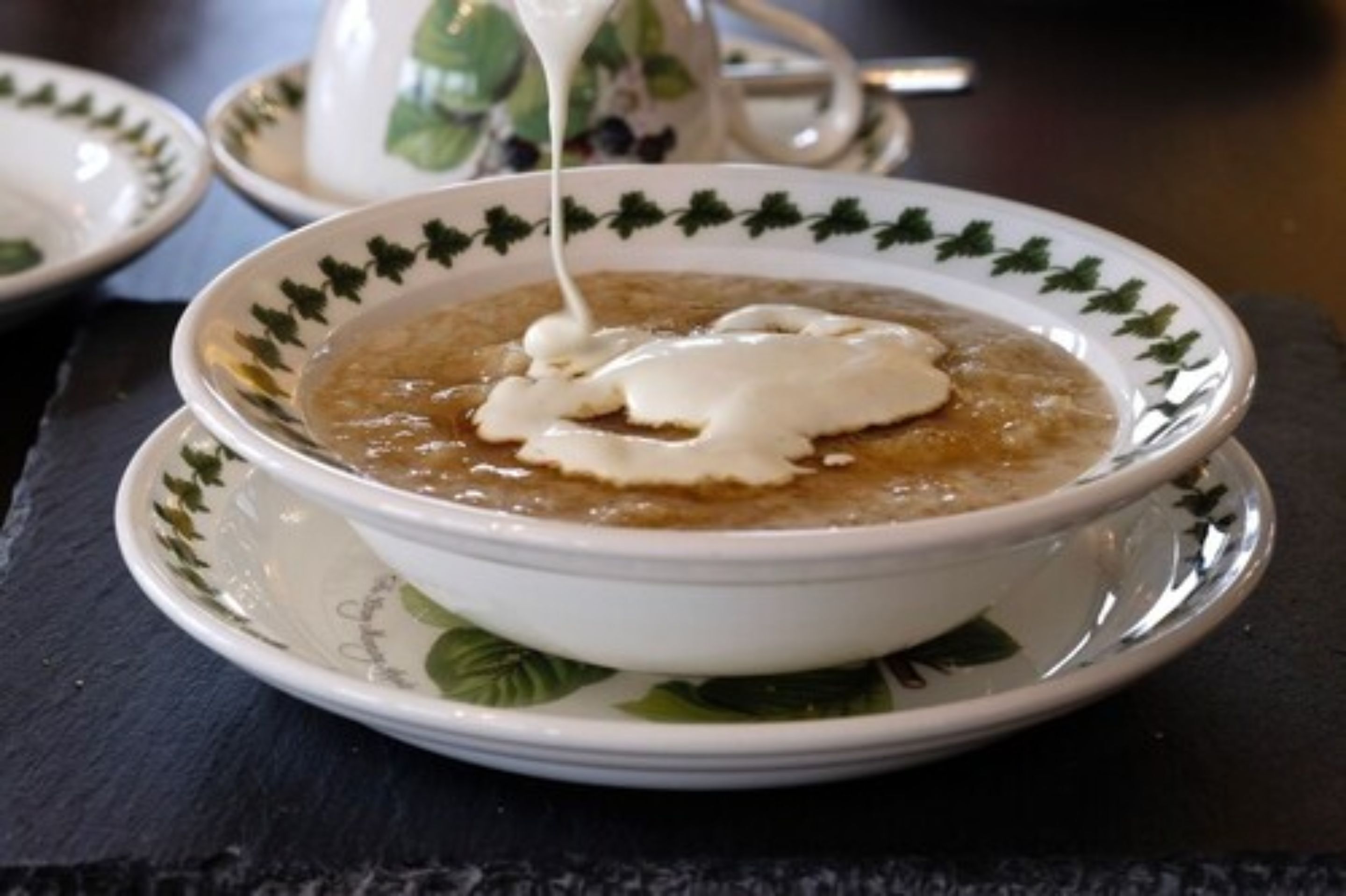 A bowl of soup with a creamy topping, served on a white plate with a green leaf pattern.