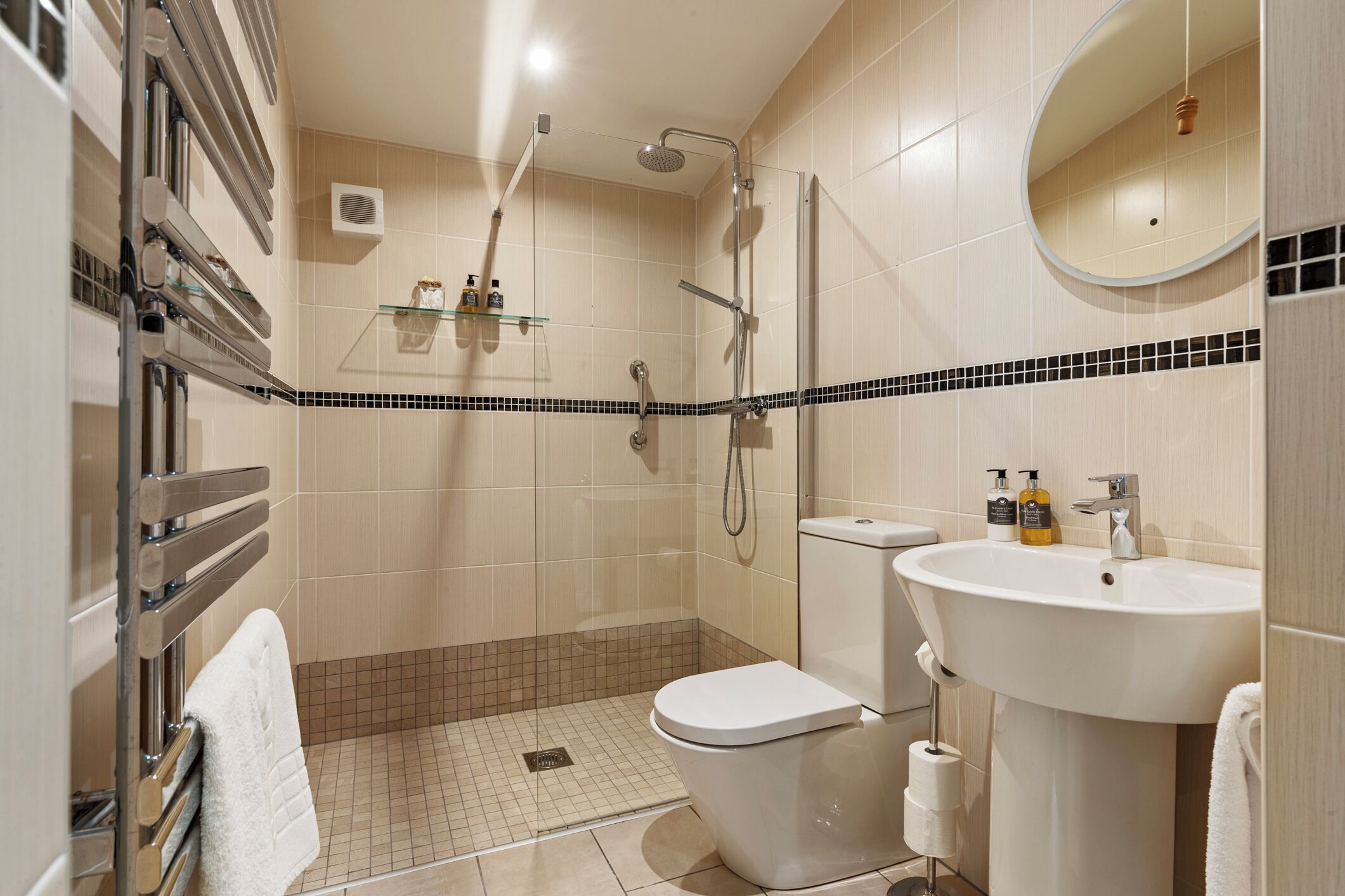 Un baño moderno con ducha, inodoro, lavamanos y un estante de vidrio con artículos de aseo.