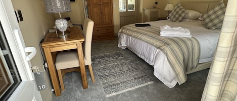 A bedroom with a bed, a desk, a chair, a wardrobe, and a door leading to another room.