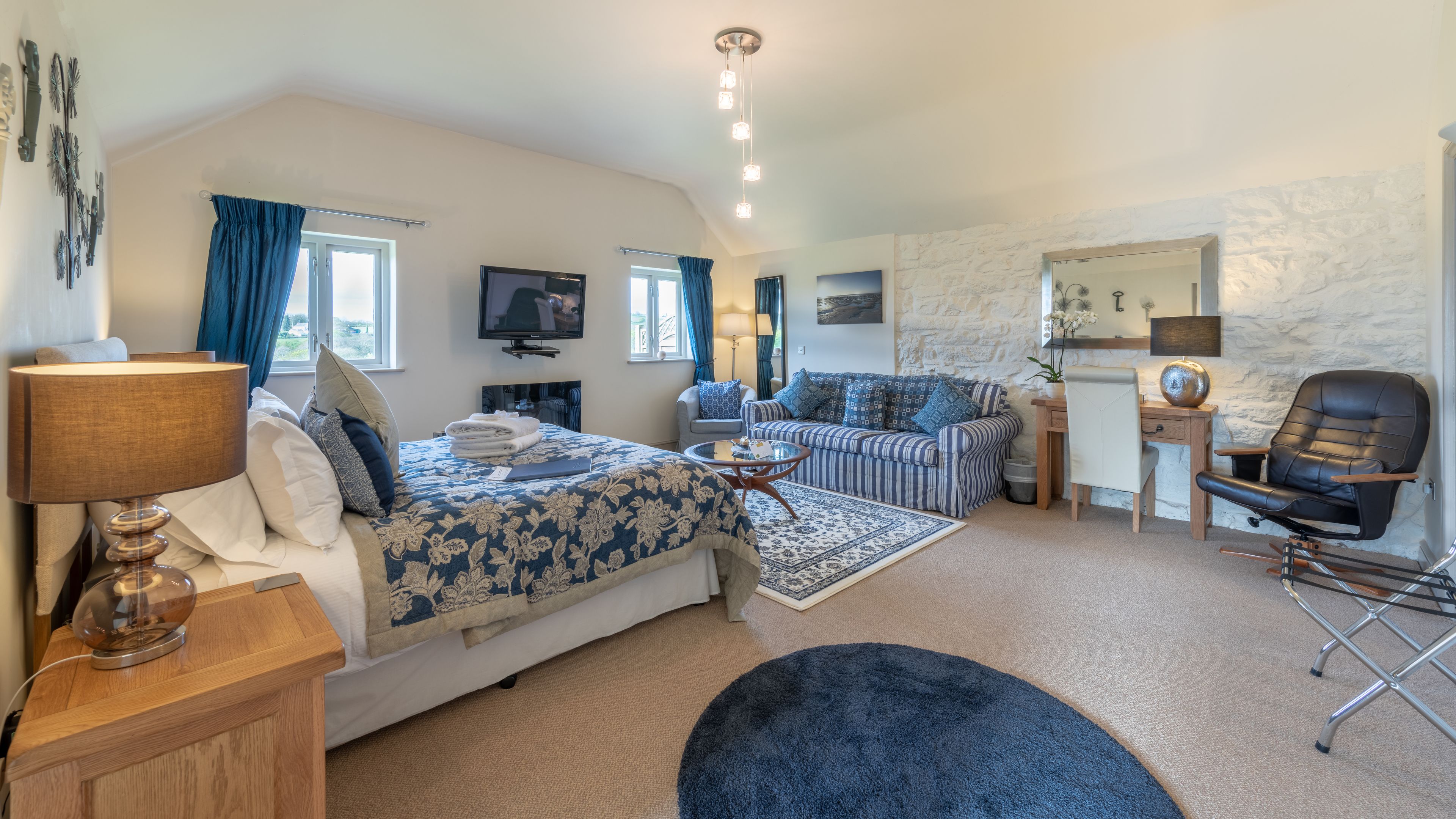 A bedroom with a bed, a sofa, a desk, a chair, a TV, and a lamp.