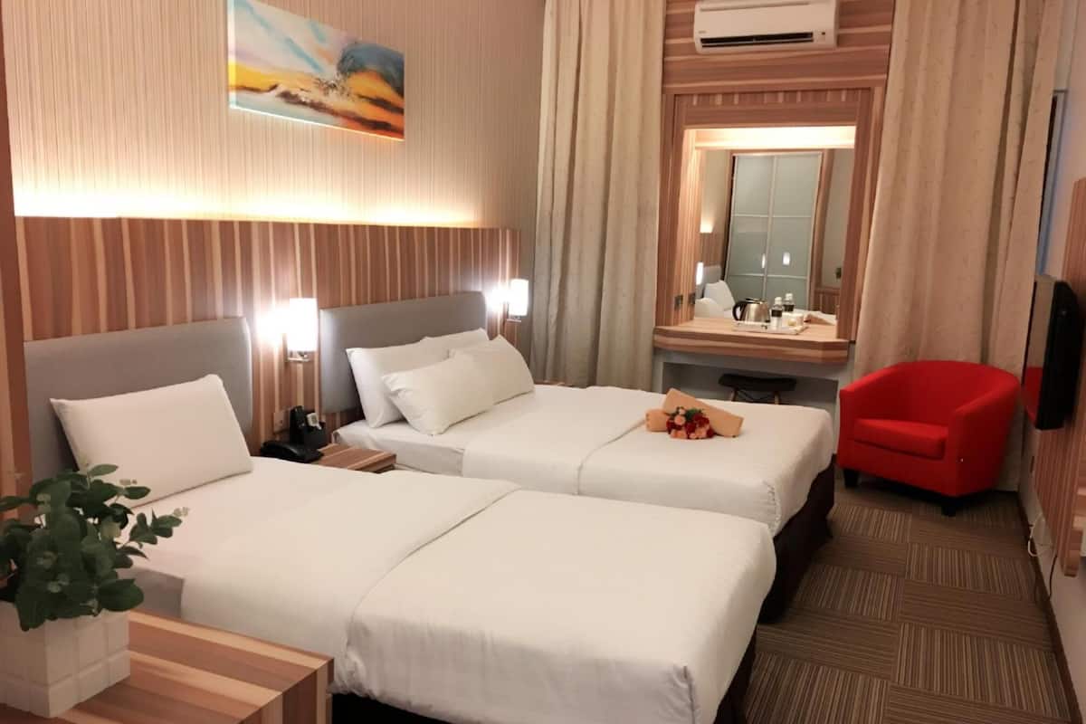 A hotel room with two beds, a desk, a red chair, a mirror, and an air conditioning unit.