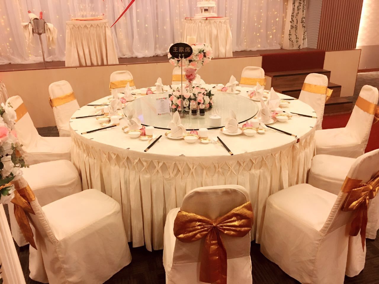 A round table with white tablecloths and gold sashes, surrounded by chairs with similar sashes.