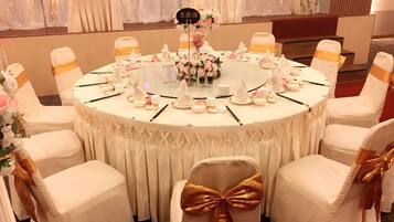 A round table with white tablecloths and gold sashes, surrounded by chairs with similar sashes.