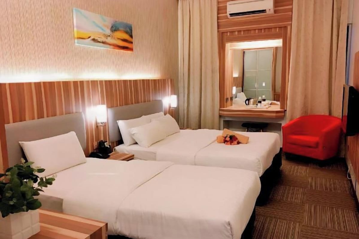 A hotel room with two beds, a desk, a chair, a mirror, and an air conditioning unit.