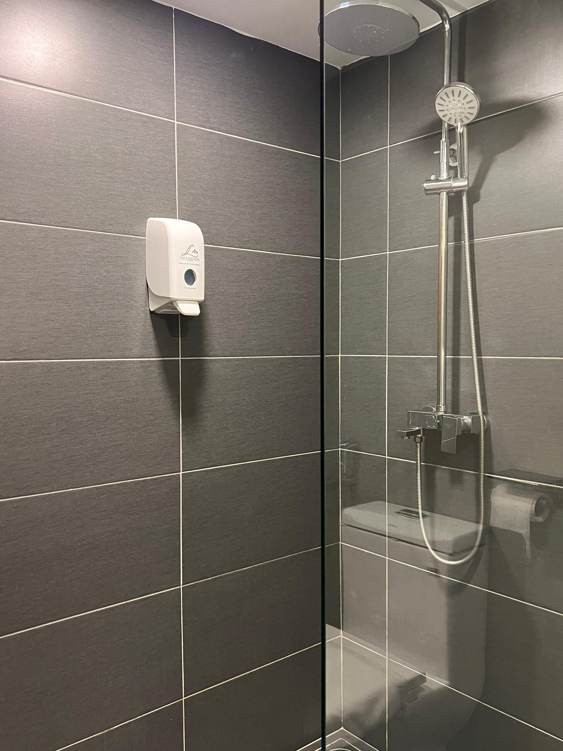 Una ducha moderna con cabezal de ducha de mano y dispensador de jabón de mano fijado a la pared.