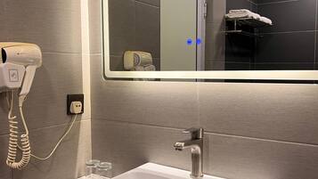 A modern bathroom with a large mirror, a white sink, a hairdryer, and a towel rack.