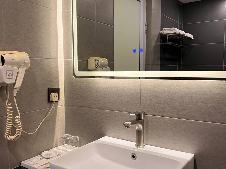 A modern bathroom with a large mirror, a white sink, a hairdryer, and a towel rack.