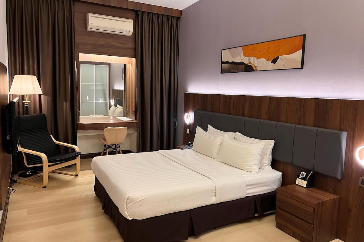 A hotel room with a large bed, a desk with a chair, a TV, and a bedside table with a lamp.