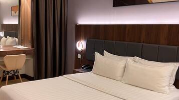 A hotel room with a large bed, a desk with a chair, a mirror, and a wall-mounted air conditioner.