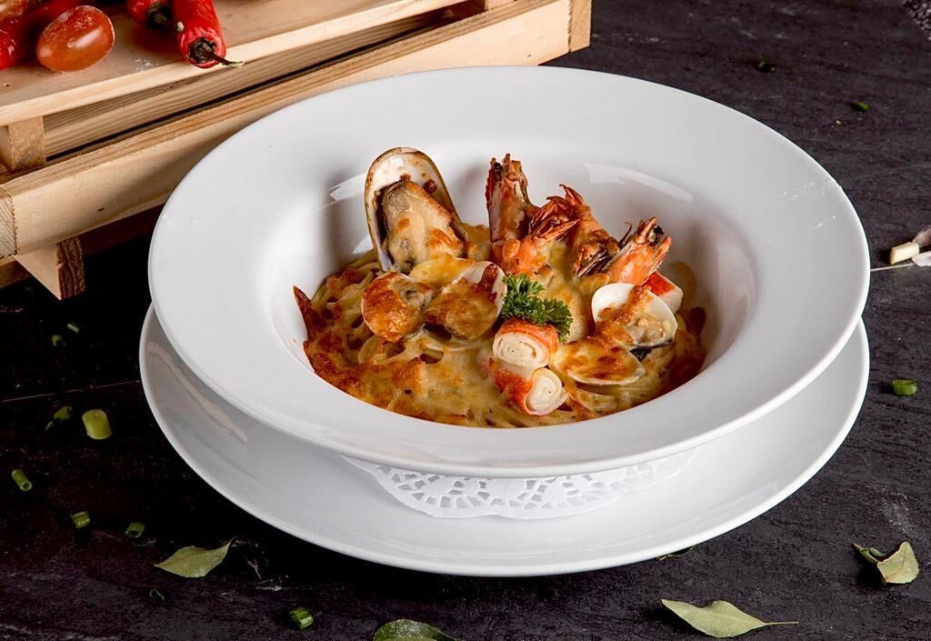 A bowl of seafood pasta with shrimp and clams, garnished with parsley, on a white plate.