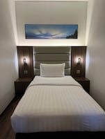 Habitación de hotel con una cama grande, dos mesitas de noche con lámparas, cabecero y un cuadro enmarcado sobre la cama.