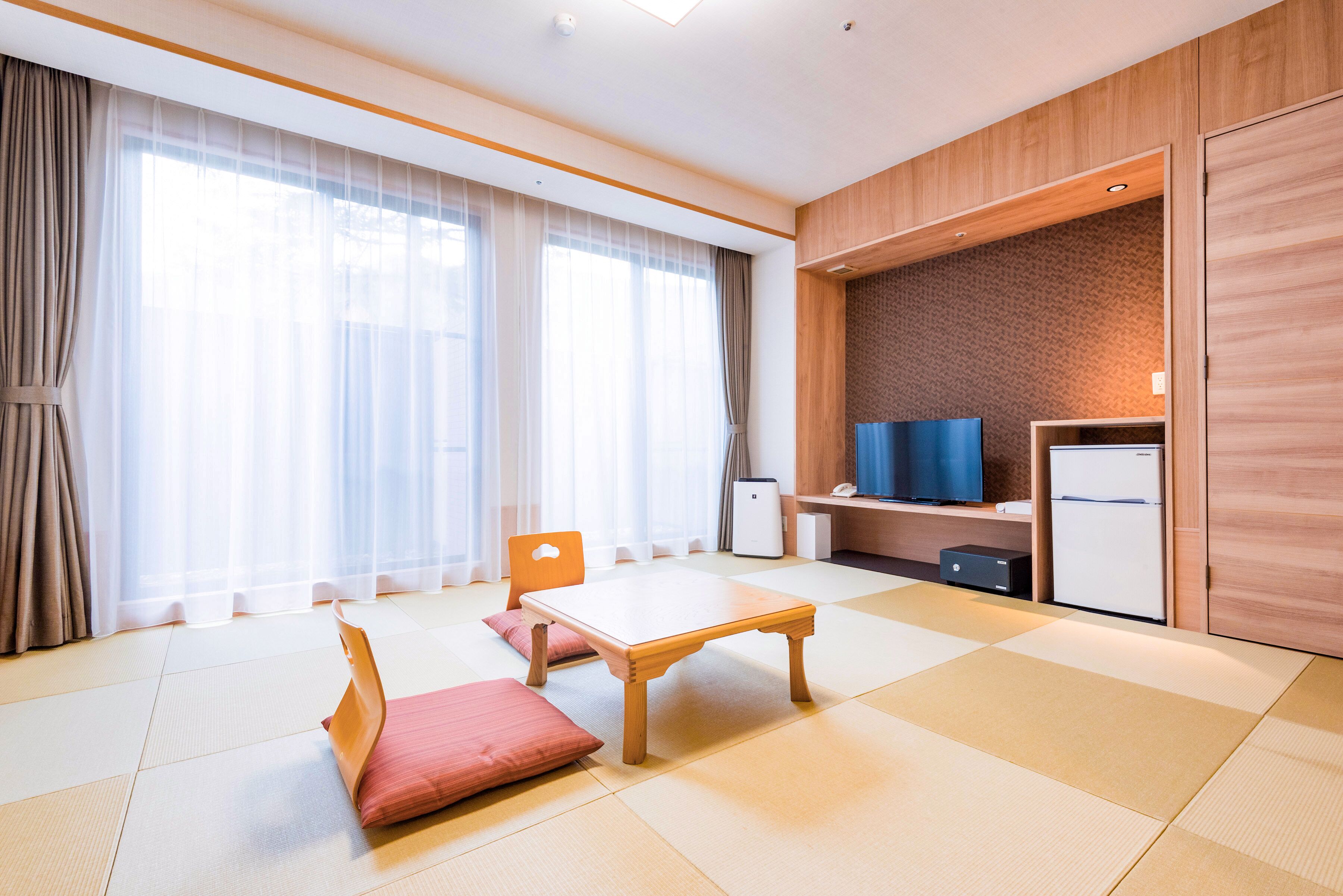 Una habitación de hotel moderna con suelo de tatami, una mesa de madera, un sofá, un televisor y un refrigerador pequeño.