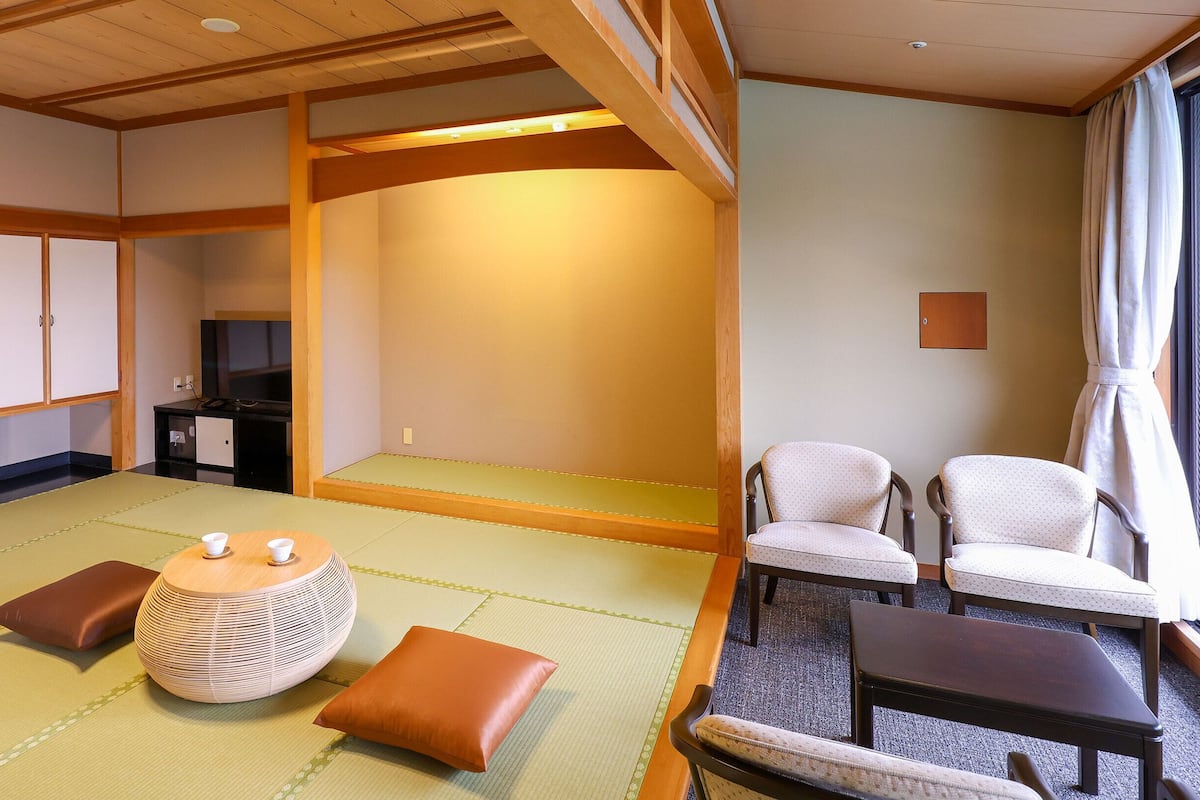 A traditional Japanese room with tatami flooring, a low table with cushions, and two chairs.