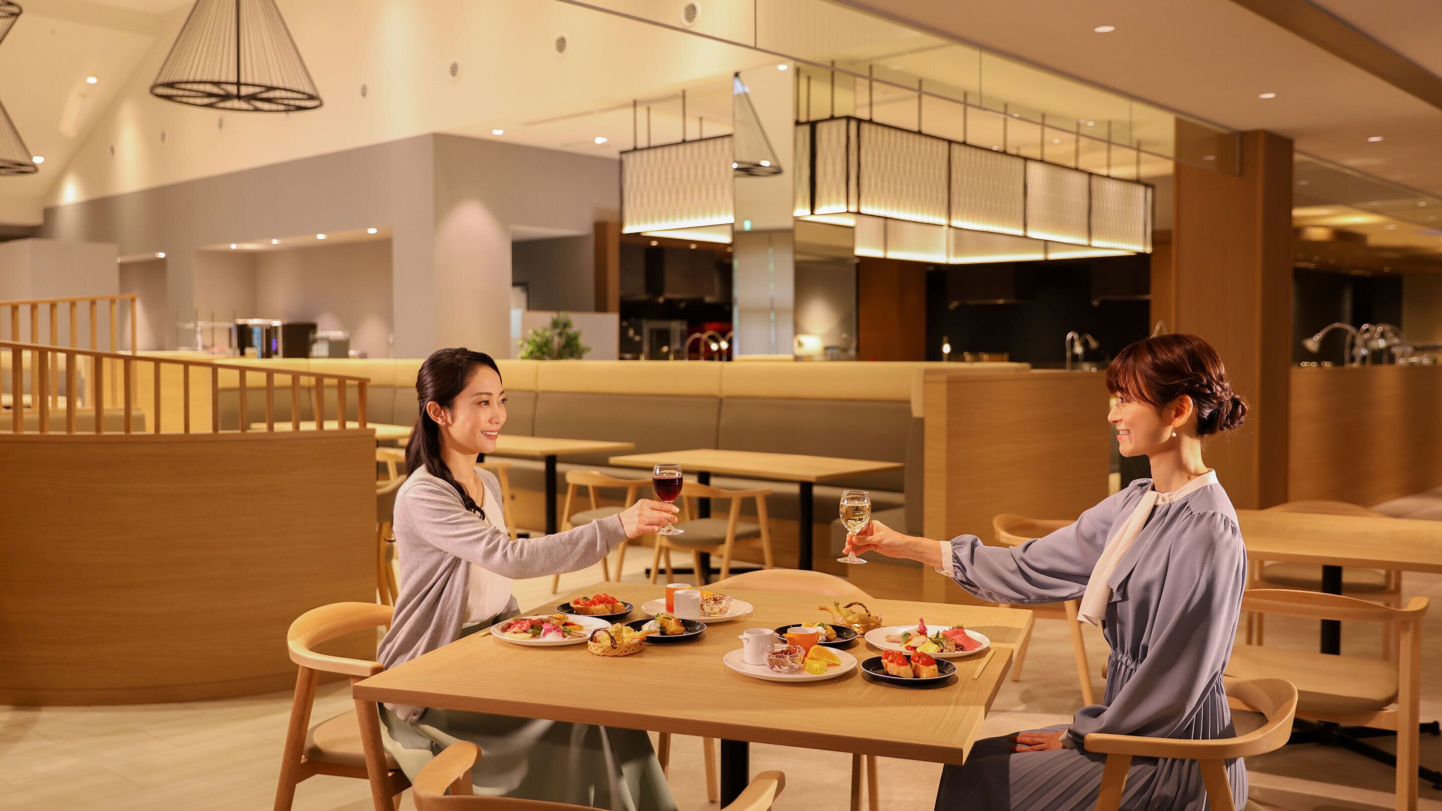 Un espace repas moderne avec des tables et des chaises en bois, une variété de plats disposés sur les tables et un design intérieur contemporain agrémenté de luminaires suspendus.