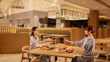 A modern dining area with wooden tables and chairs, a variety of dishes on the tables, and a contemporary interior design with pendant lighting.