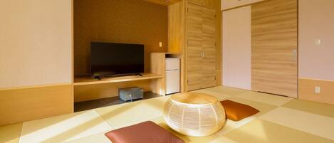 A modern hotel room with a television, a small refrigerator, and a futon bed with cushions.