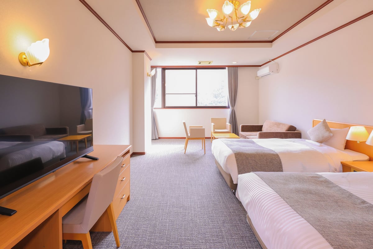 A hotel room with a large bed, a desk with a TV, a chair, and a window with curtains.