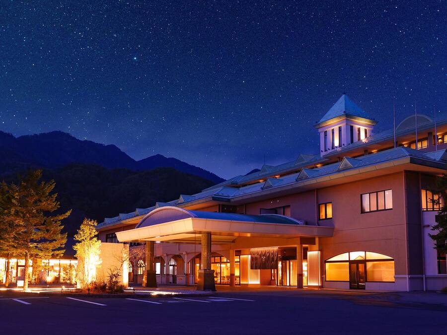 A hotel with a covered entrance, a bell tower, and a mountain backdrop.