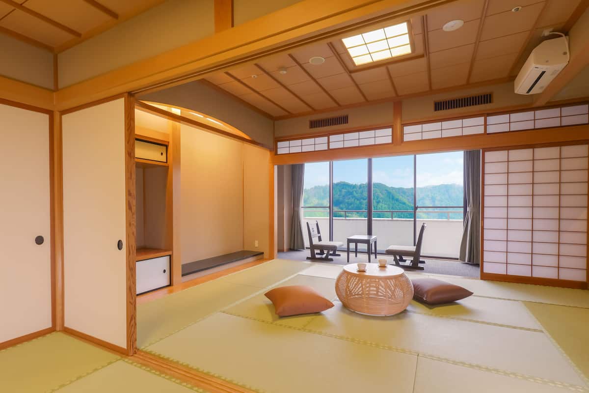 A traditional Japanese room with tatami flooring, a low table with cushions, and a view of mountains through large windows.