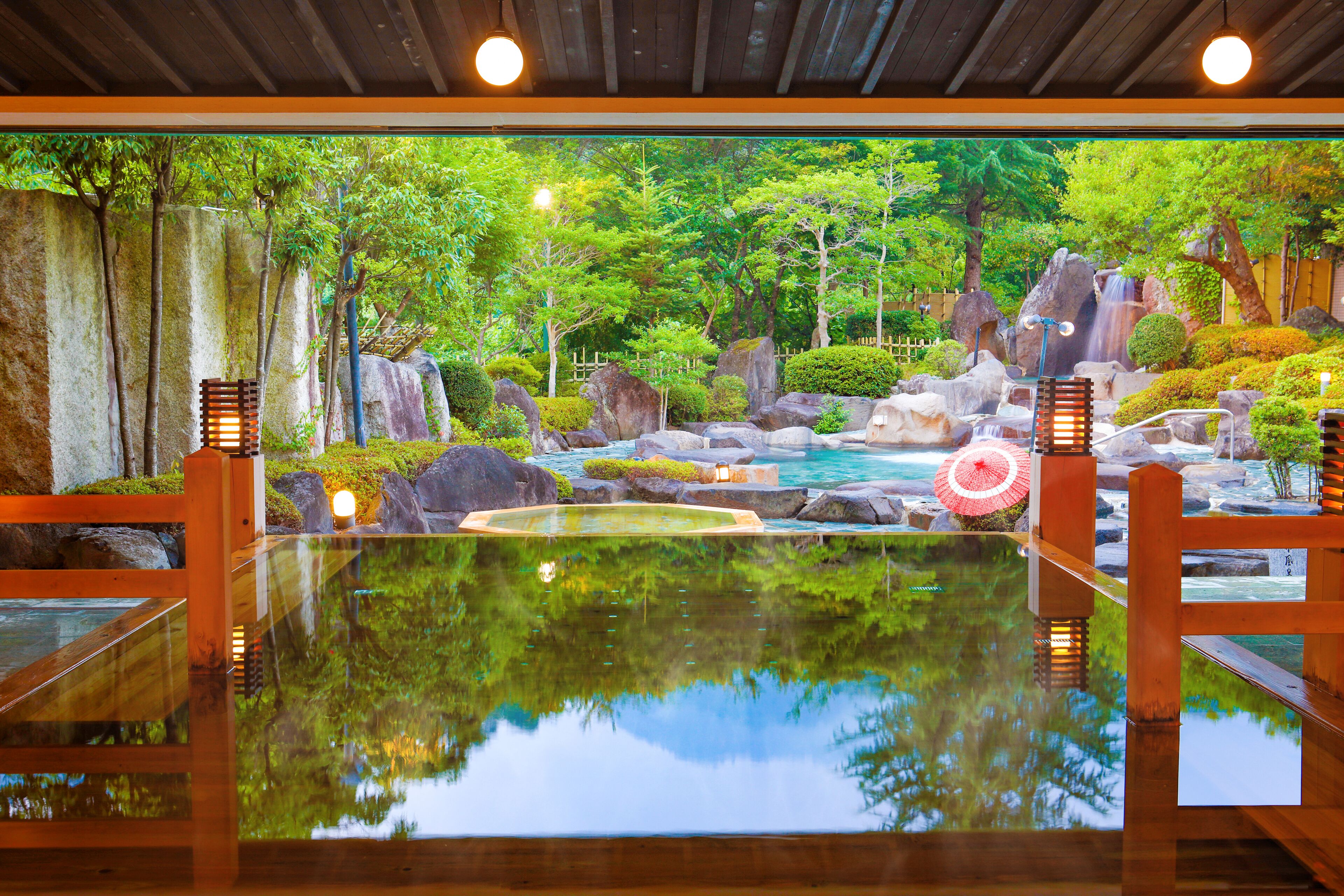 Un jardín interior tranquilo con un estanque reflectante, bancos de madera y una cascada de fondo.