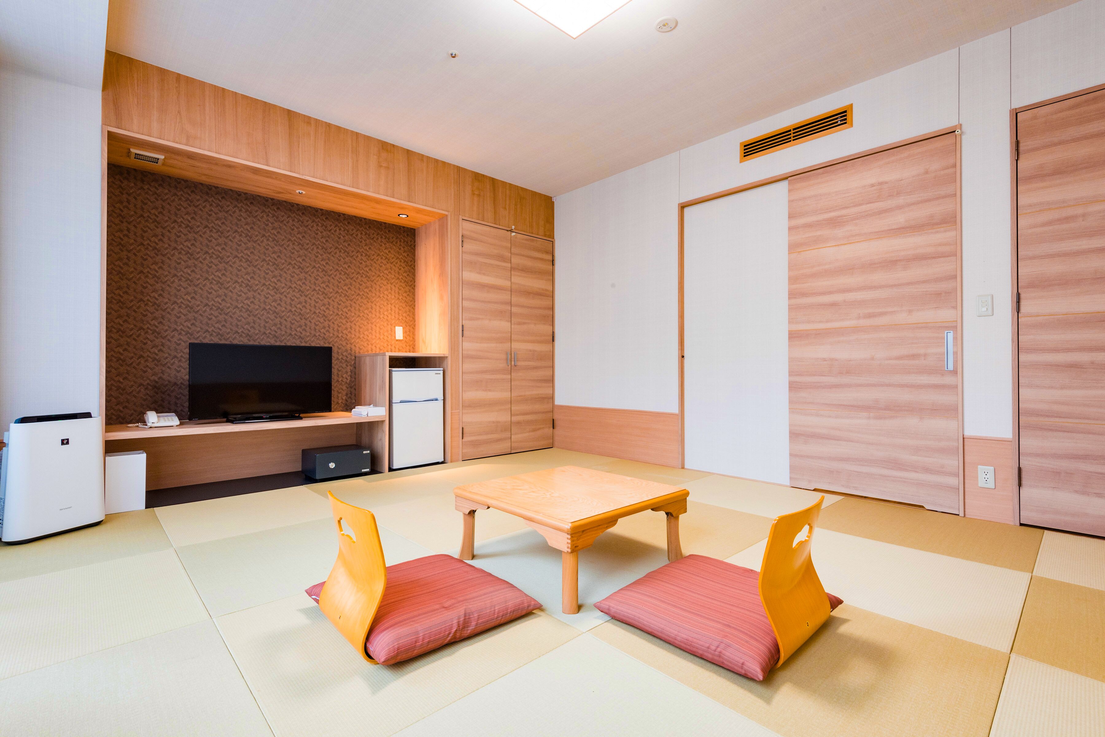 A modern room with a flat-screen TV, a small refrigerator, a wooden cabinet, and a tatami mat floor.