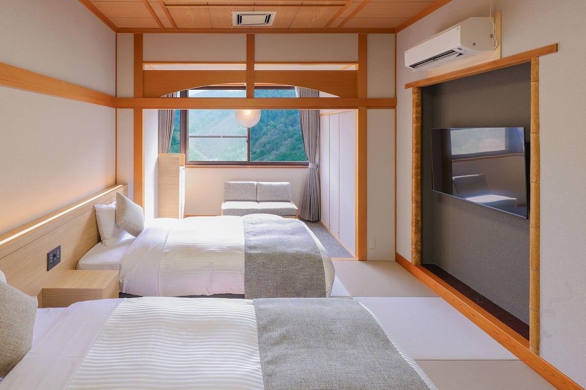 A hotel room with two beds, a TV, and a window with a view of the outdoors.