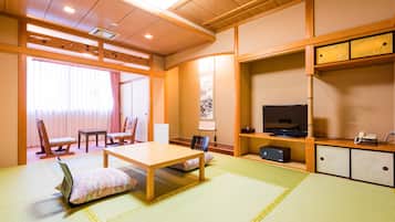 Traditional Japanese-style room with tatami flooring, featuring a low table, TV, and cabinet.