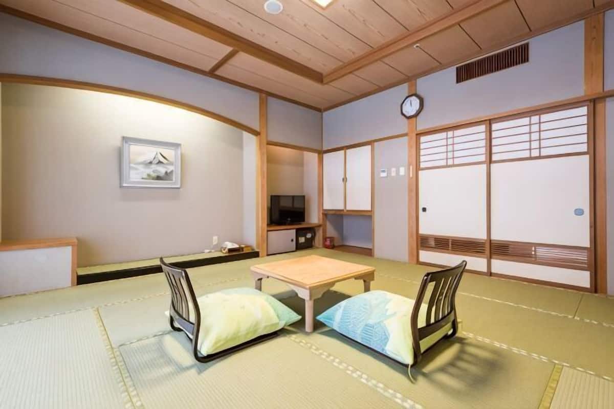 A traditional Japanese room with tatami flooring, a low table, two cushions, a television, and sliding doors.