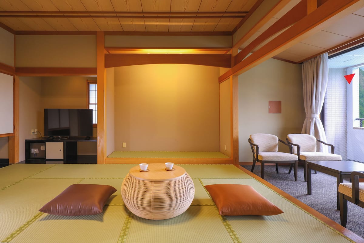 A traditional Japanese room with tatami flooring, a low table with cushions, a television, and a sliding door.