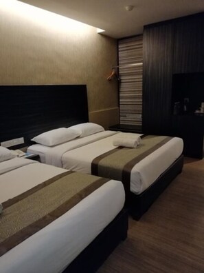 Hotellihuone, jossa on kolme sänkyä, tumma pääty, suuri peili ja puulattia.