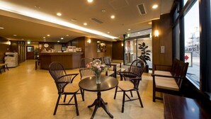 A hotel lobby with a reception desk, seating area with round tables and chairs, and large windows offering a view of the street. - Iidaya (Matsumoto)
