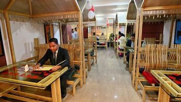 Un restaurante con mesas y cabinas de madera, una persona leyendo la carta y otros comensales al fondo.