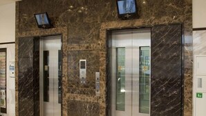 Un vestíbulo con dos ascensores, paredes de mármol y una pantalla de televisión sobre cada uno.