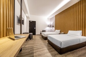 Una habitación de hotel moderna con un escritorio de madera, dos camas, una silla, una maleta y un televisor en la pared.