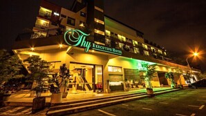 Een hotel met een modern ontwerp, met een opvallend bord 'Thy Executive Hotel', een goed verlichte ingang en een parkeerplaats.