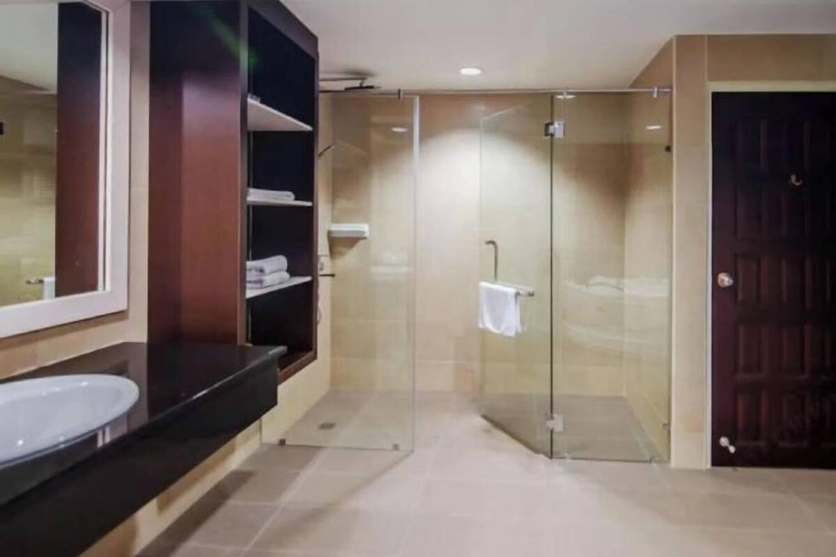 A bathroom with a glass-enclosed shower, a large mirror, and a dark wooden vanity.