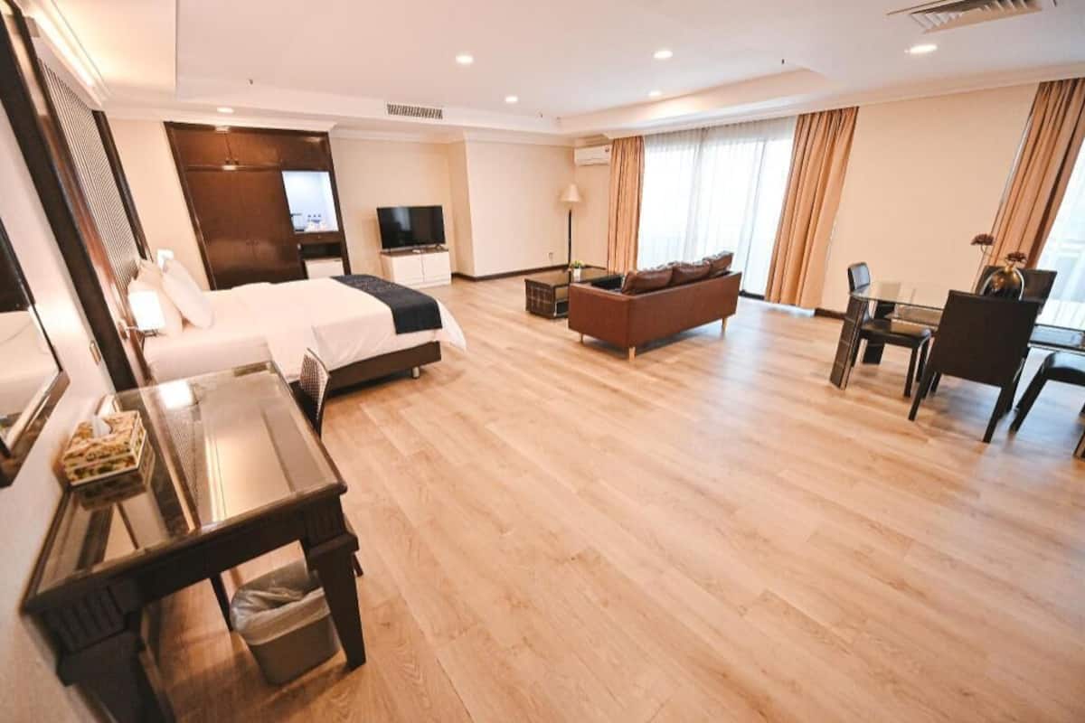 A hotel room with a bed, a TV, a sofa, a dining table, and a chair.