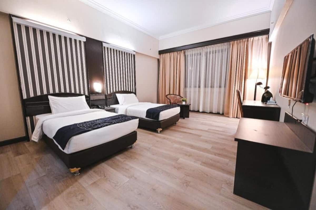 A hotel room with two beds, a desk, a chair, a TV, and a window with curtains.