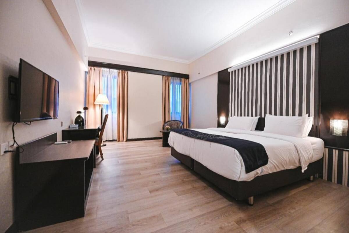 A hotel room with a bed, desk, chair, TV, and curtains.