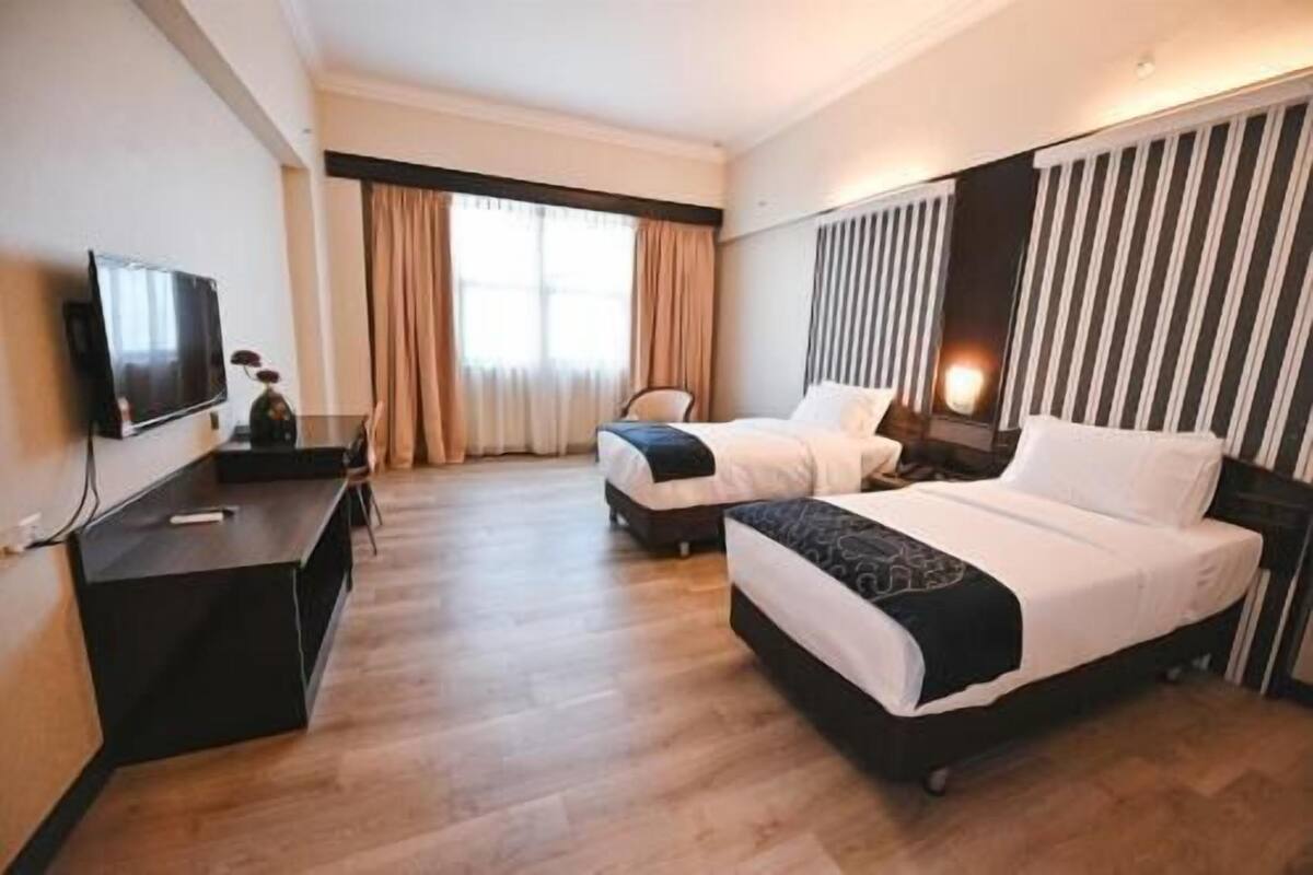 A hotel room with two beds, a desk, a TV, and a window with curtains.